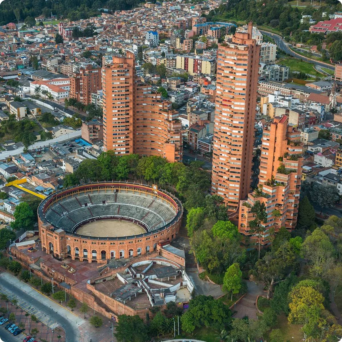 Aerial view of Bogota, Colombia showing a large circular bullring surrounded by tall orange apartment buildings and green trees.