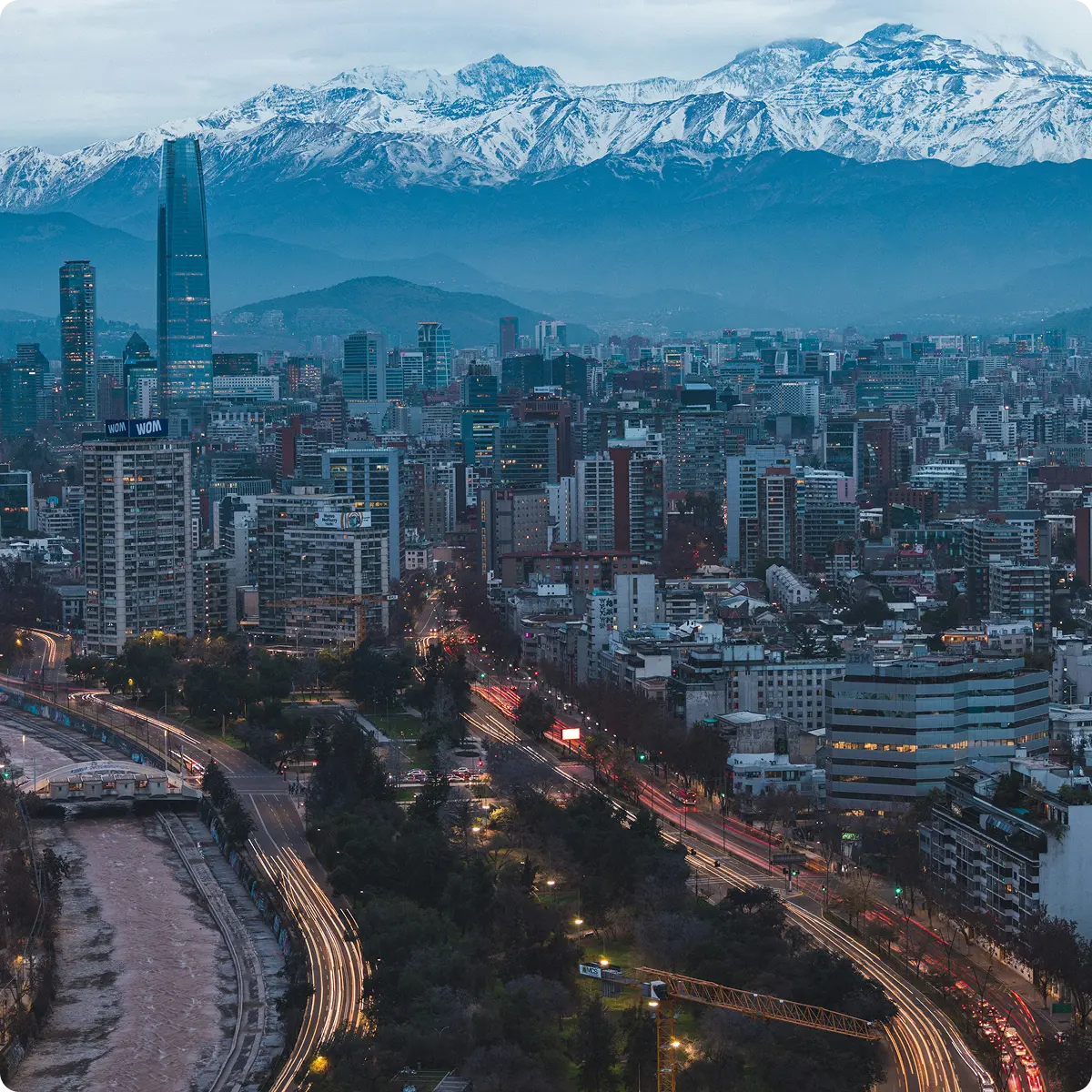 Evening skyline of Santiago, Chile with tall buildings, busy streets and snow-capped Andes mountains in the background.