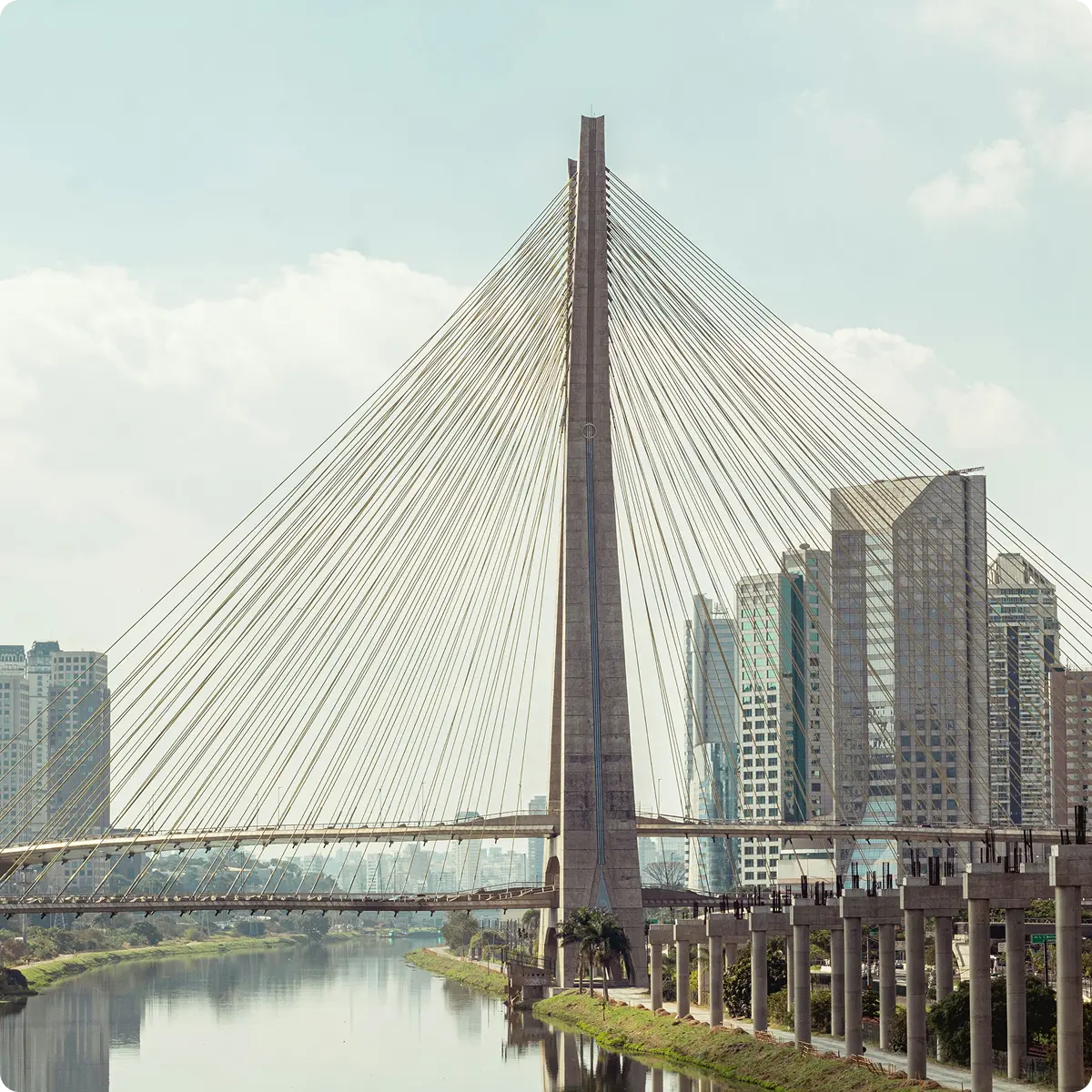 Cable-stayed bridge over a calm river with modern high-rise buildings in the background under a partly cloudy sky.