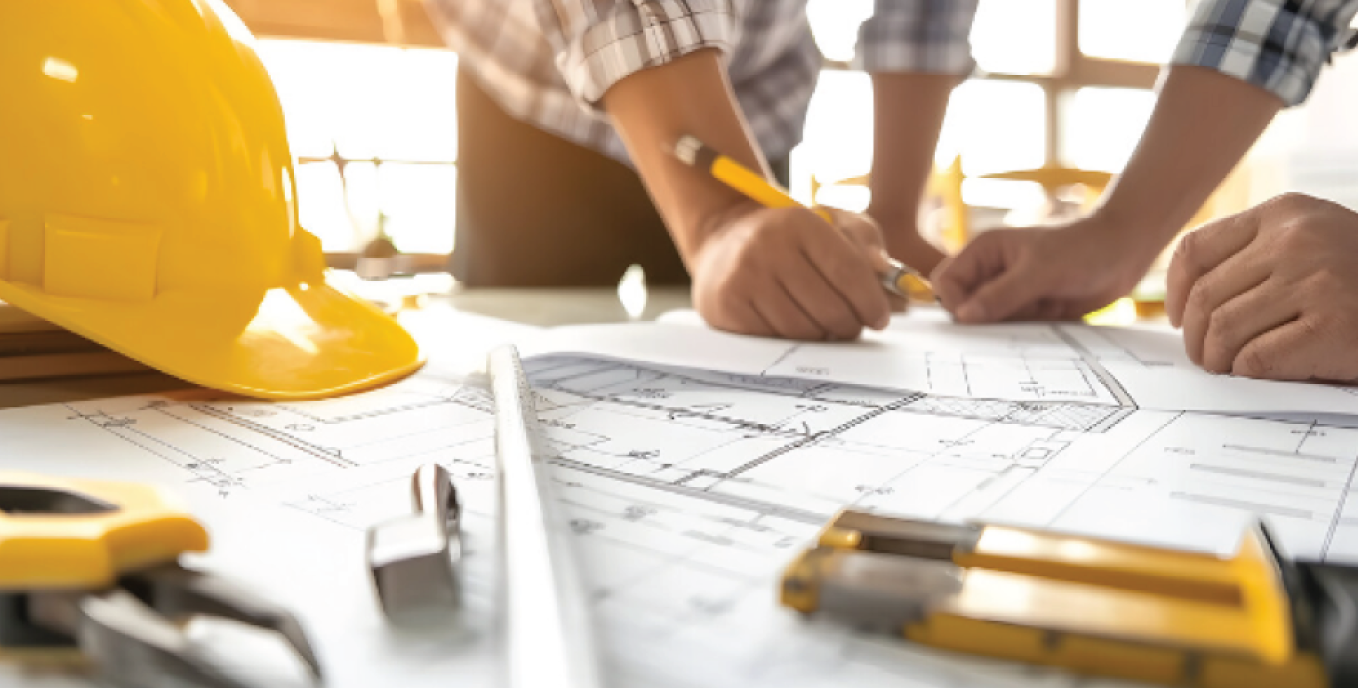 Personen arbeiten an einem architektonischen Bauplan auf einem Tisch mit Bauhelm und Werkzeugen.