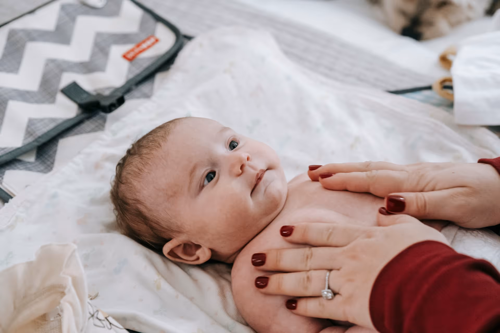 Infant lying on a blanket with adult hands gently touching the baby's chest.