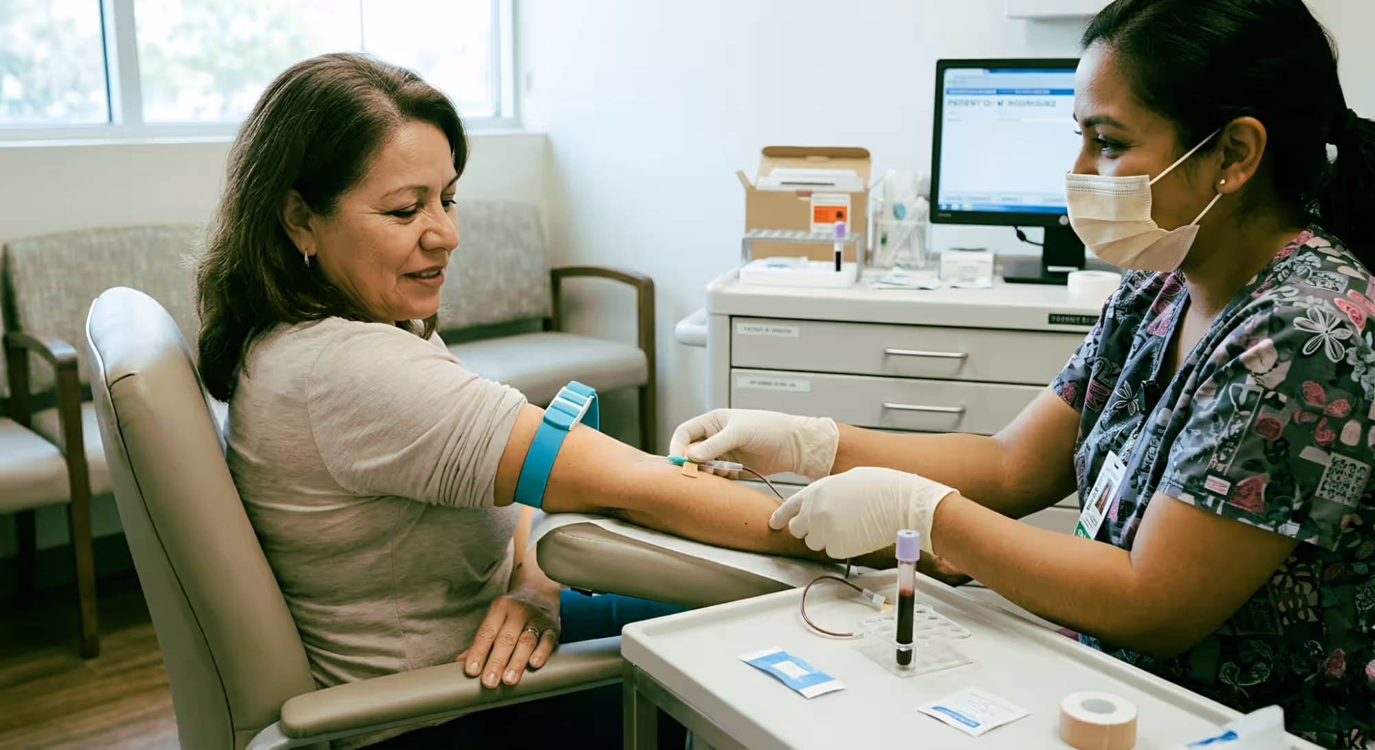 Nurse wearing gloves and a mask drawing blood from a seated woman's arm in a clinical setting.