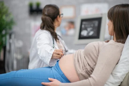 Pregnant woman lying on examination table during ultrasound check with female doctor.