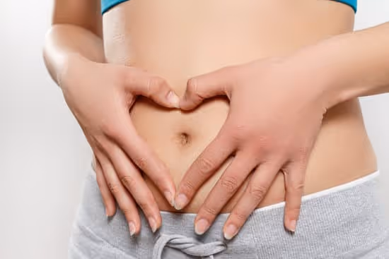 Woman making a heart shape with hands over her bare stomach.