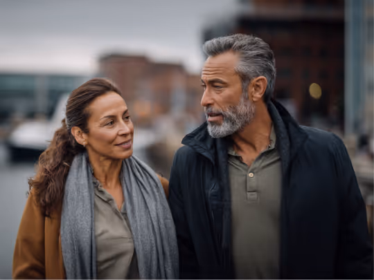 Middle-aged couple wearing coats walking outdoors in an urban setting while looking at each other.