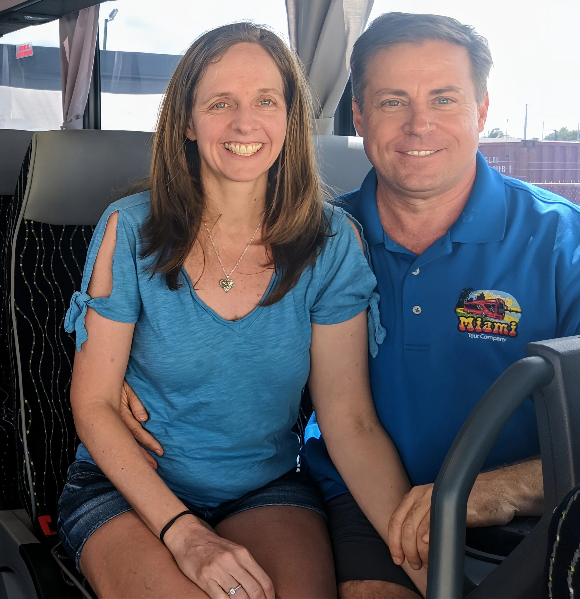 Michelle and Gus Moore seated in the front seat of a bus holding hands.