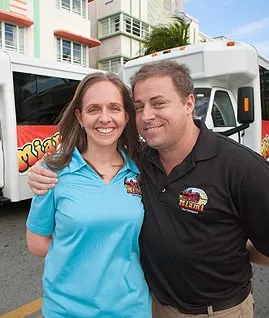 a smiling Michelle and Gus Moore standing near the buses