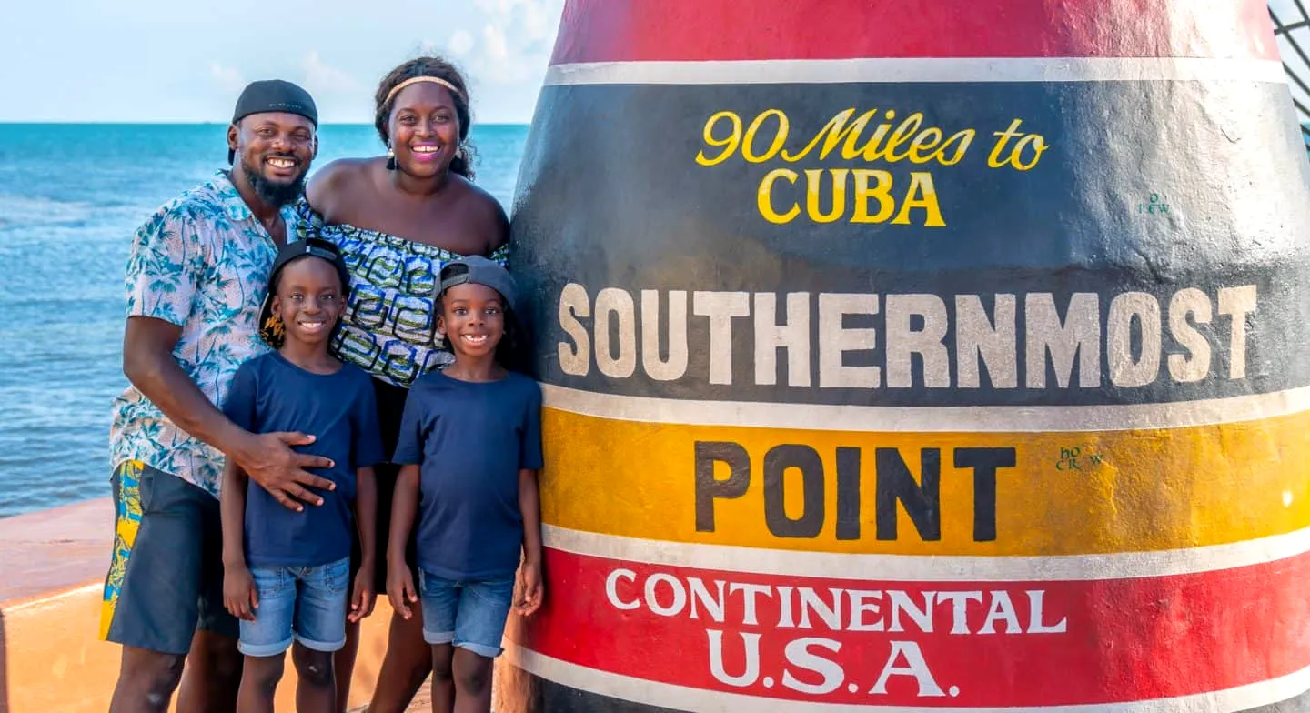 Attractive black family taking a group photo at Southermost Point on a sunny day.