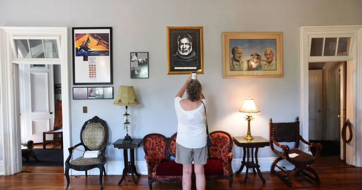 Lady in shorts taking a photo of a painting of Papa inside the Hemingway House.