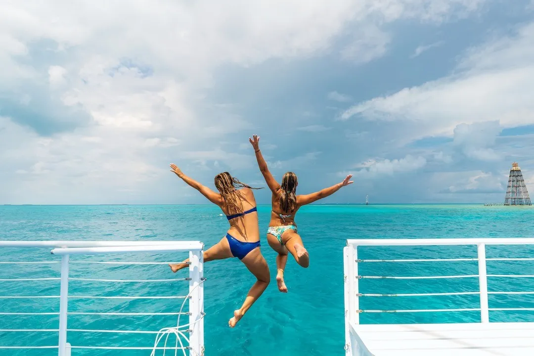 Two girls jumping off the boat with their arms in the air.