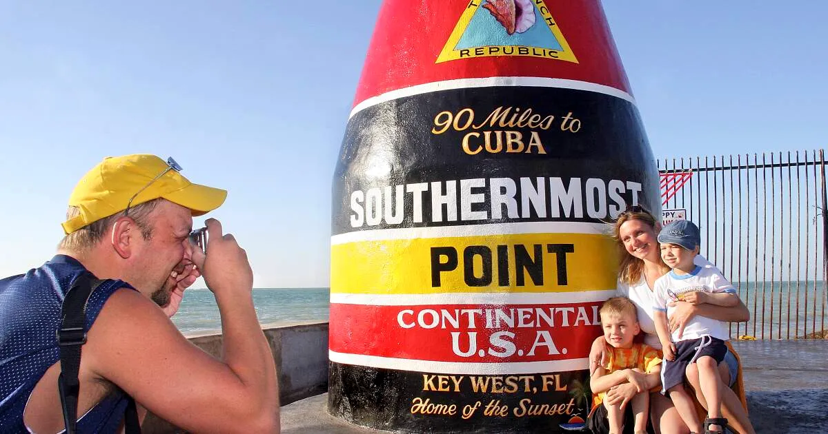 Happy white family taking a group photo at Southermost Point on a sunny day.