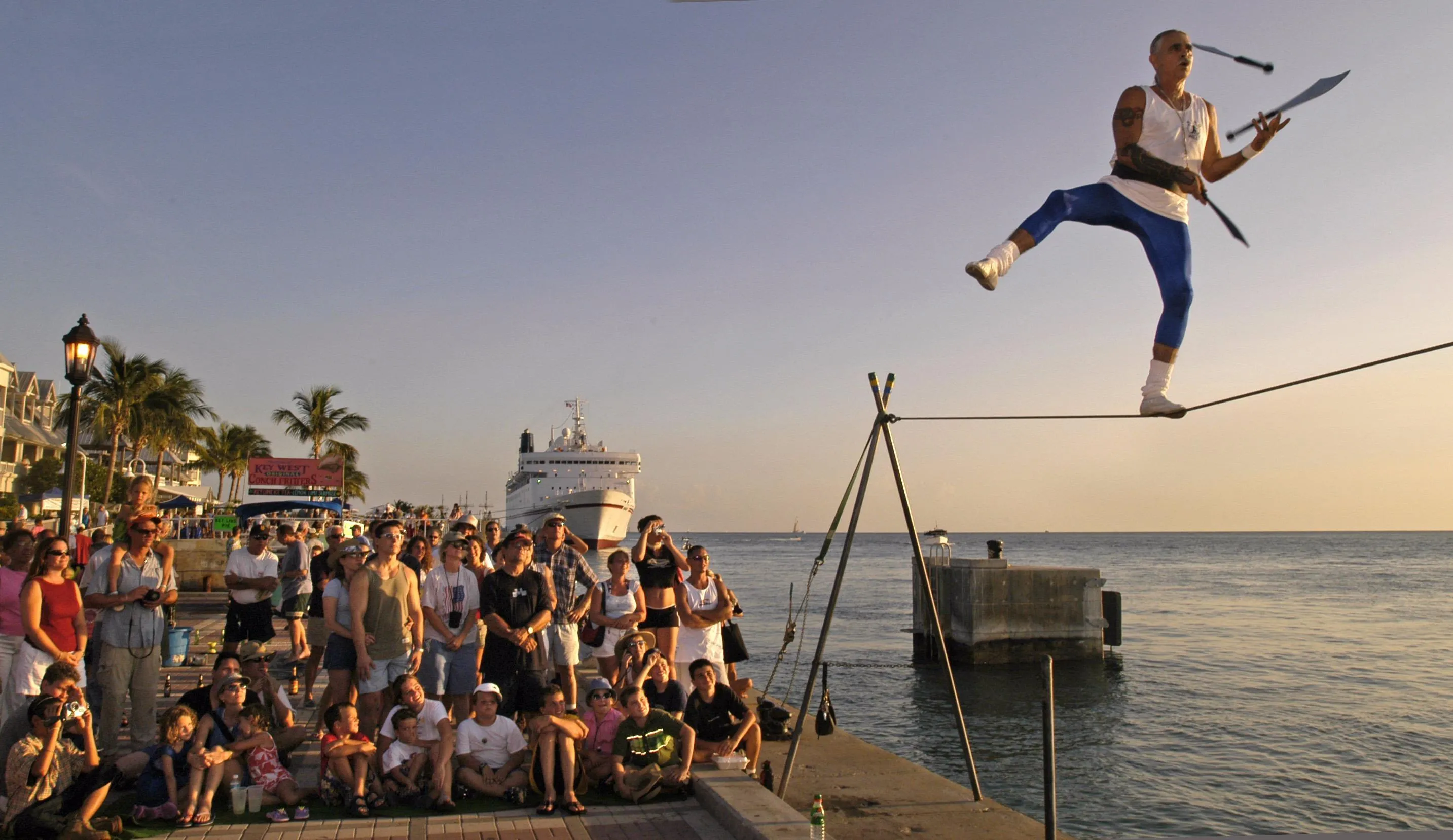 A street performer walking the tight rope while juggling for a crowd of people at Mallory Square.