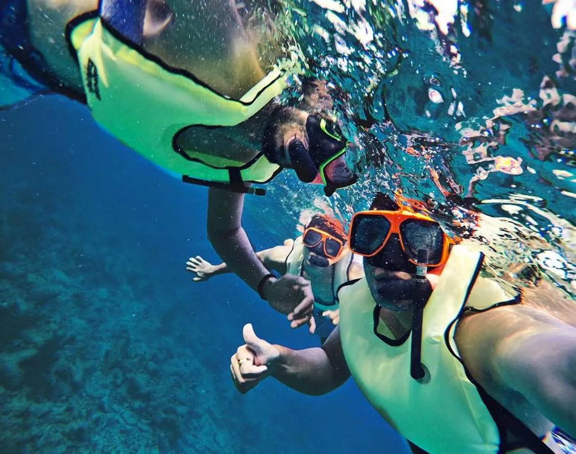 Underwater photo of a man and women looking into a coral cave with fish nearby.
