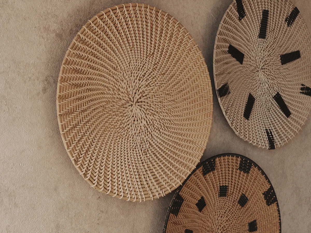 Trzy ozdobne, plecione talerze ścienne w stylu boho i etno na tle tynkowanej ściany – inspiracja do dekoracji sypialni.