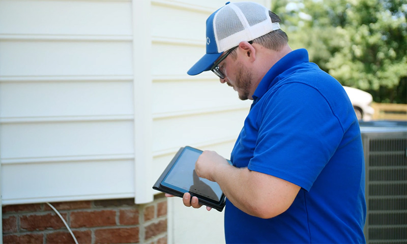Man in blue shirt and cap using a tablet outside near a building.