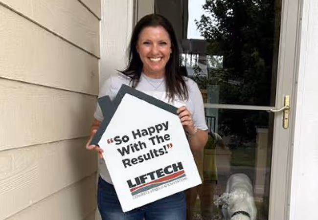 Smiling woman holding a house-shaped sign reading 'So Happy With The Results!' from LIFTECH, standing in front of a door with a dog nearby.