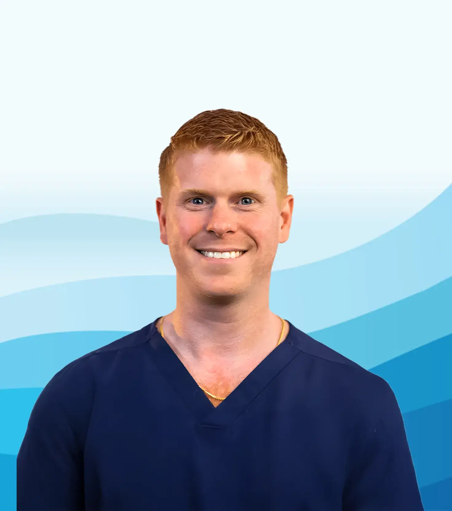 Smiling man with short red hair wearing a navy blue scrub top against a blue wave-patterned background.