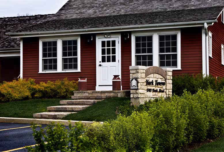A charming red house with white trim features a central white door, flanked by twin windows. 