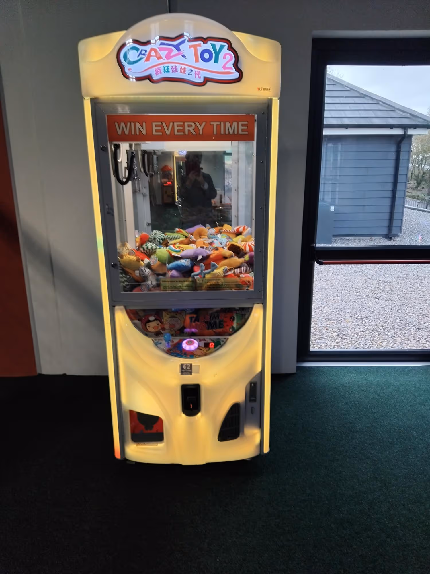 Illuminated yellow claw machine filled with various plush toys.