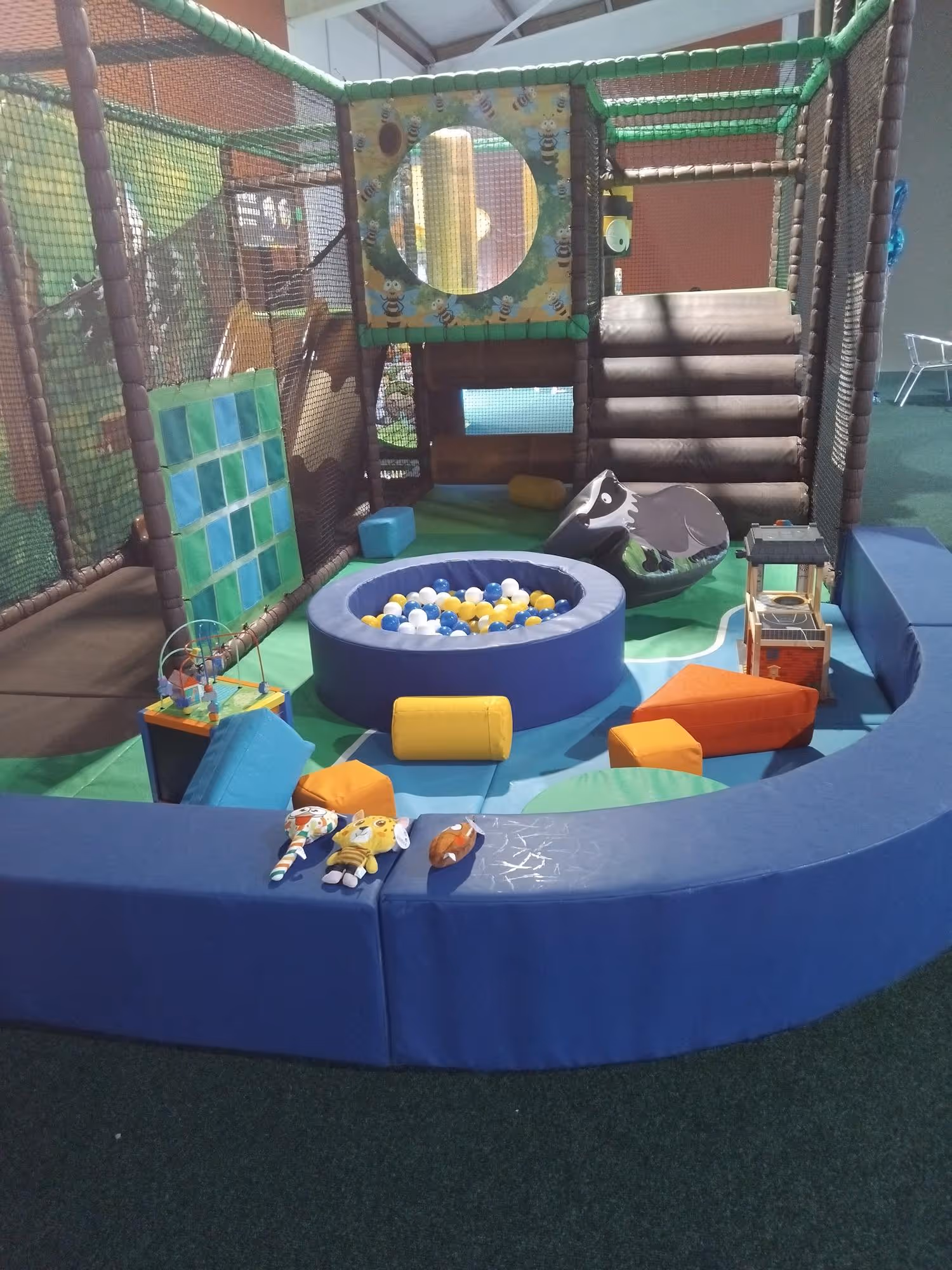 Children's play area with soft climbing structures and toys enclosed by a padded blue barrier.