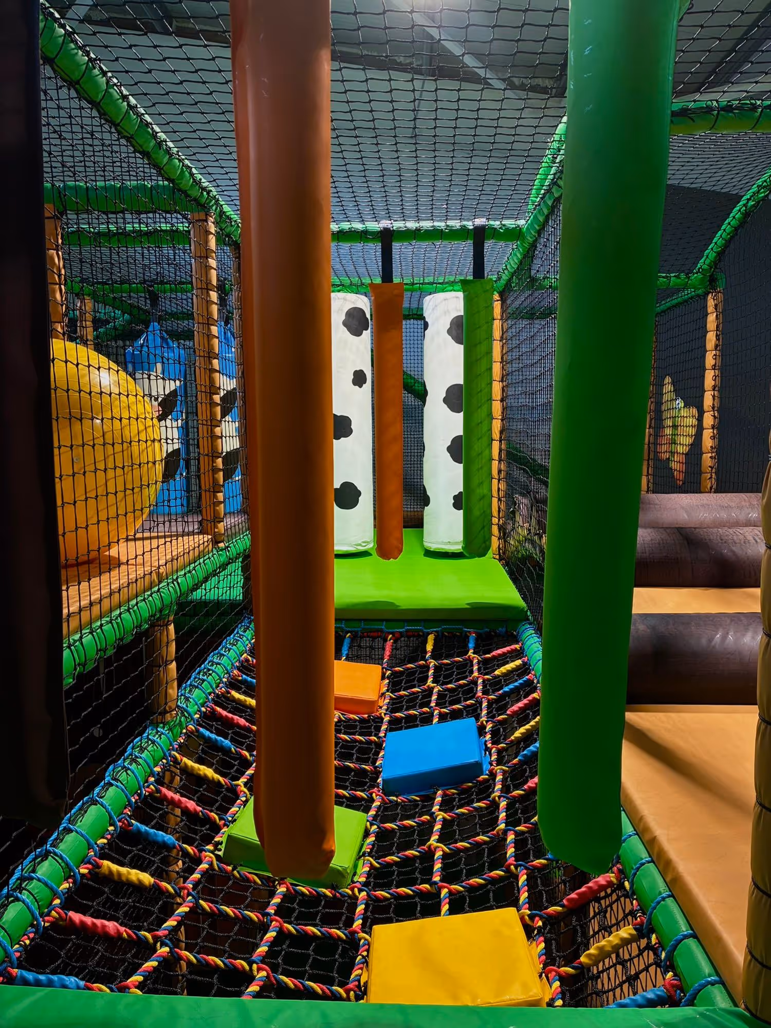 Indoor playground section with hanging padded obstacles and colorful foam blocks on a netted floor.