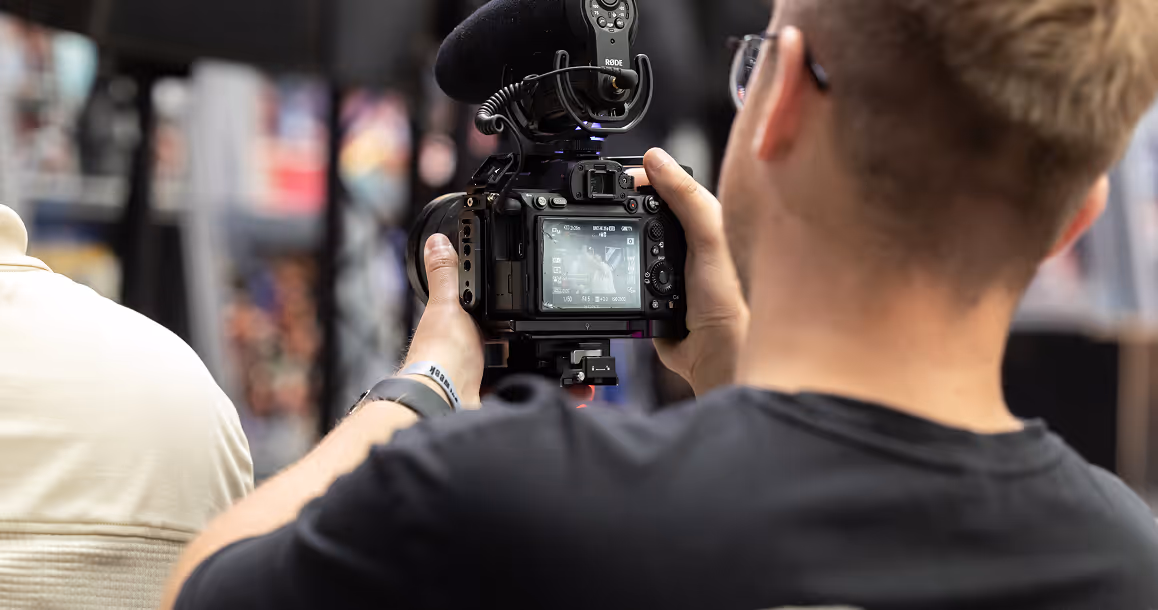 Man wearing glasses filming with a professional camera equipped with a Rode microphone.