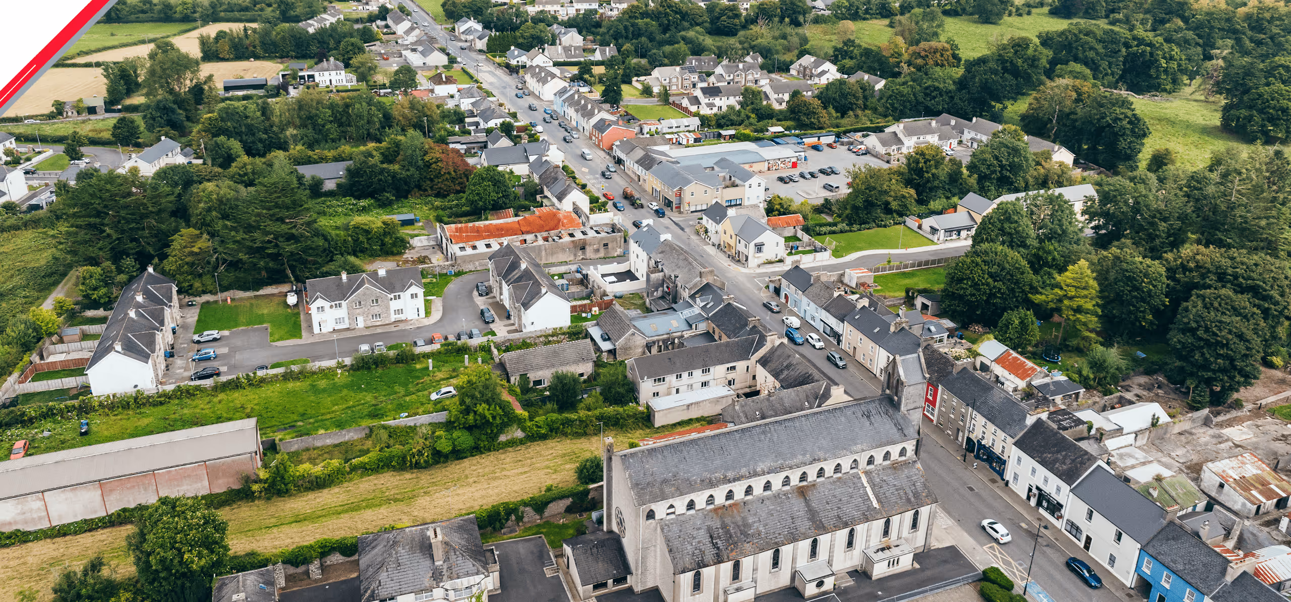 Aerial view of a small town with houses, a large church, trees, and streets with parked cars.
