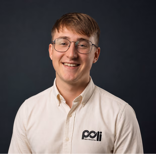 Young man wearing glasses and a light pink button-up shirt smiling at the camera.