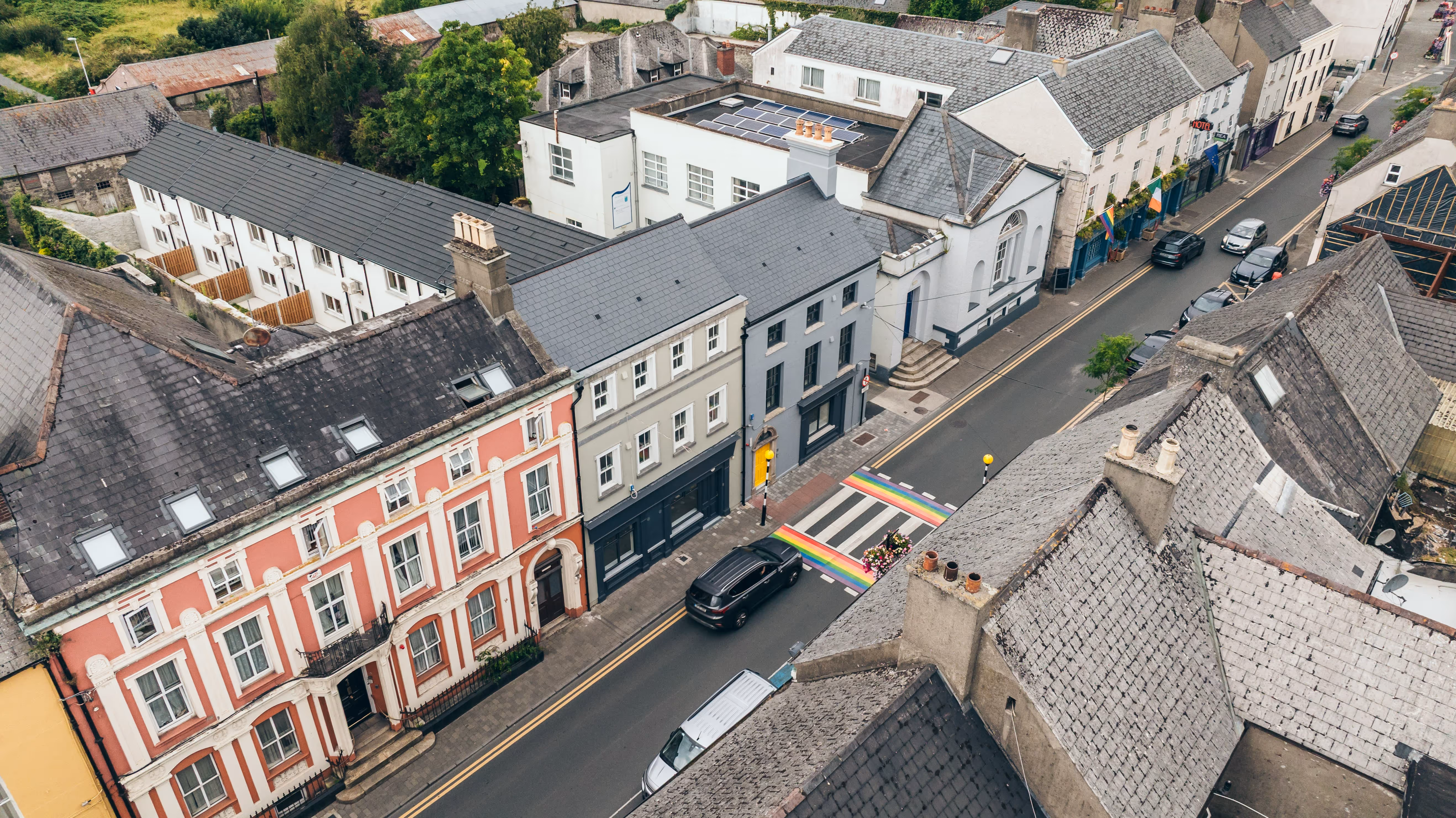Aerial view of a street with colorful buildings and a rainbow crosswalk with planted flowers.