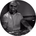 Smiling man in a short-sleeve shirt working with DJ equipment in a dimly lit setting.