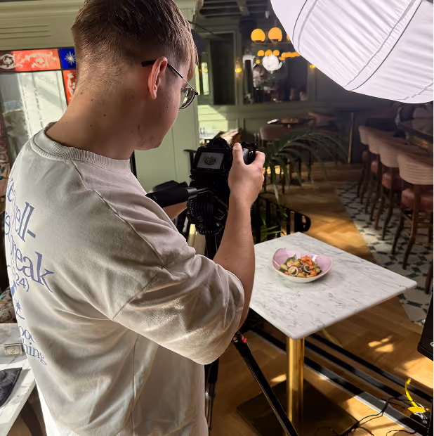 Photographer taking a photo of a salad on a marble table in a warmly lit restaurant setting.