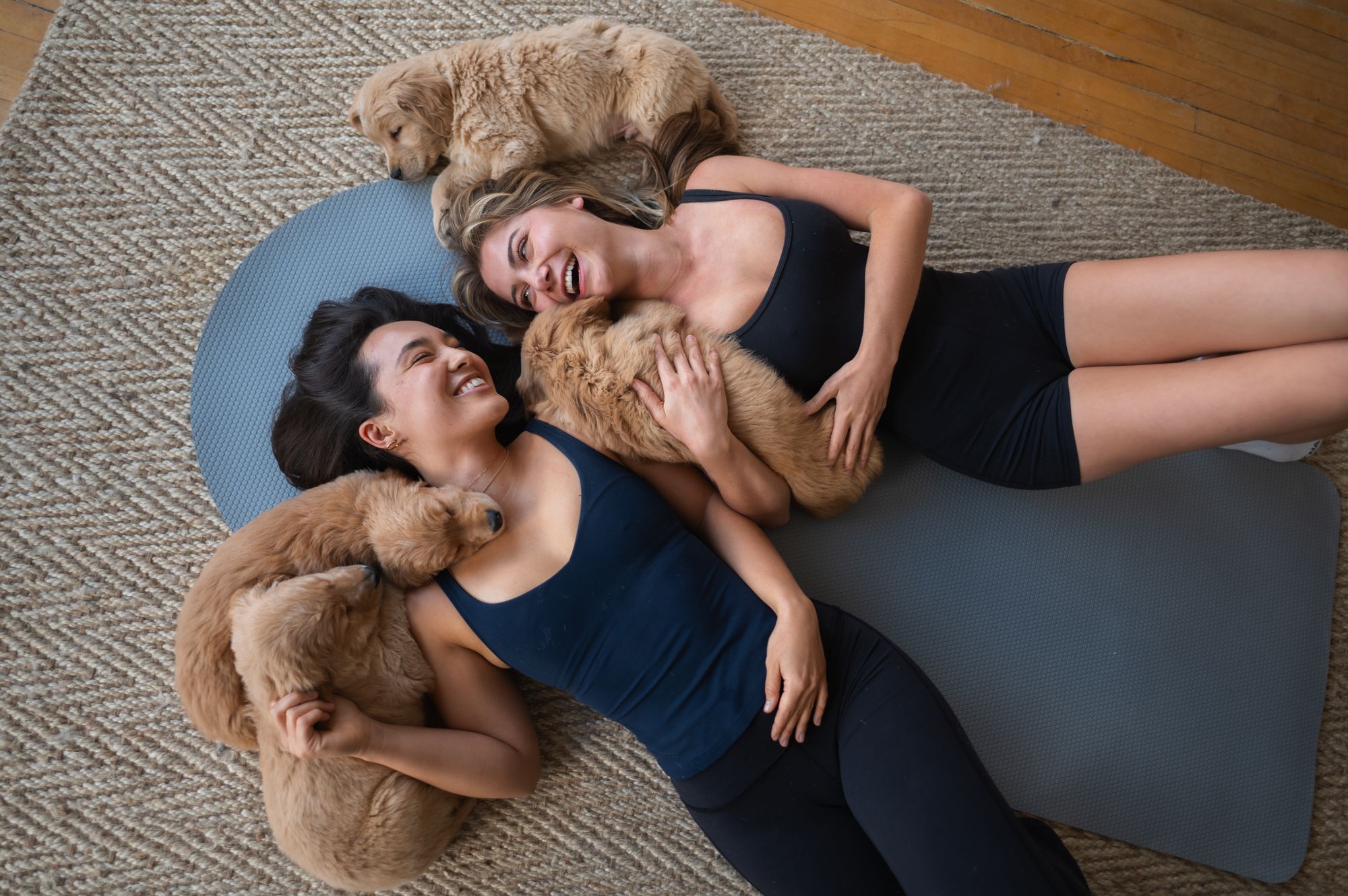 Two class participants lying on yoga mats with golden retriever puppies at a Puppy Sphere session