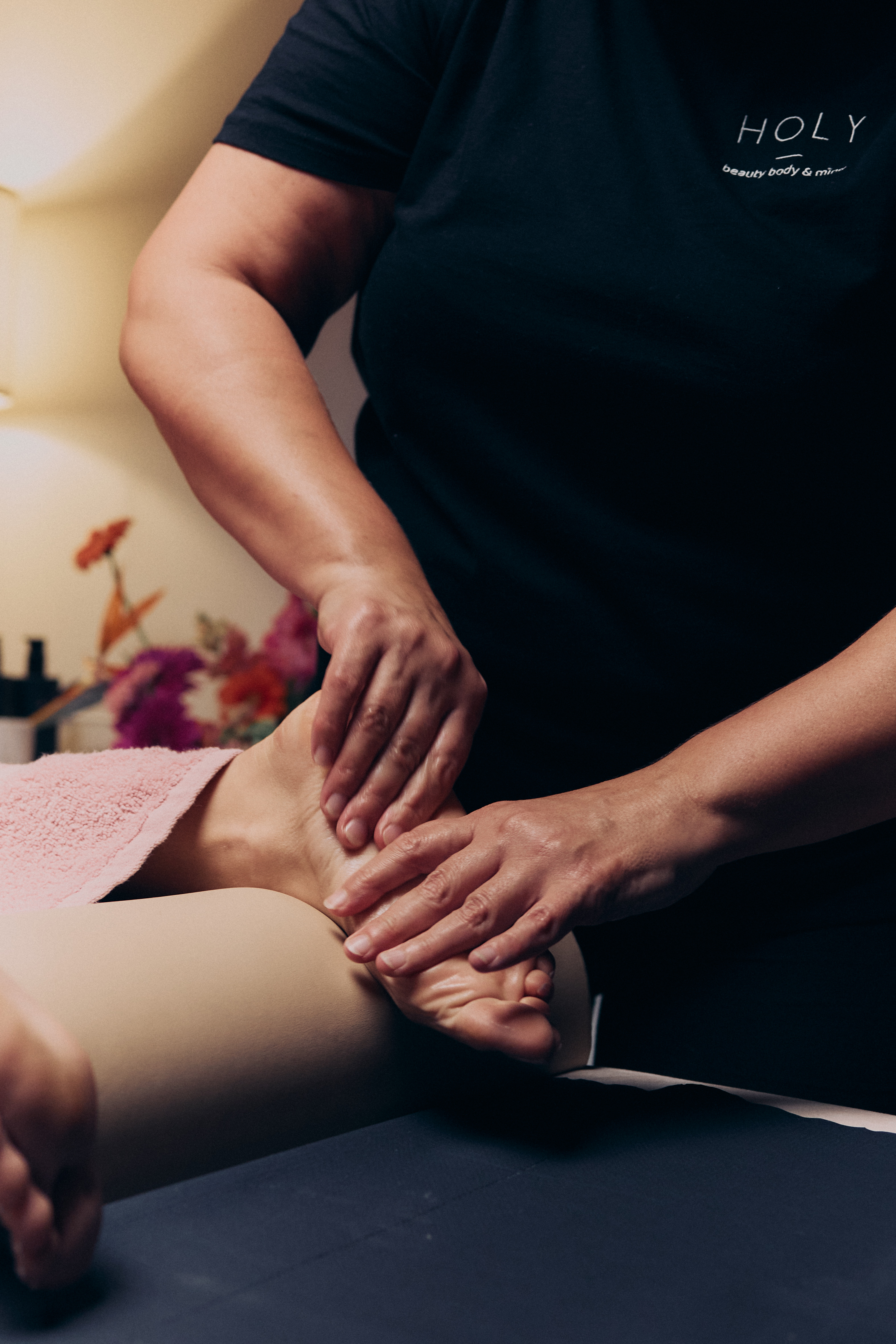 Kobieta ćwicząca rozciąganie w pozycji psa z głową w dół na macie, asystowana przez trenerkę w białej koszulce.