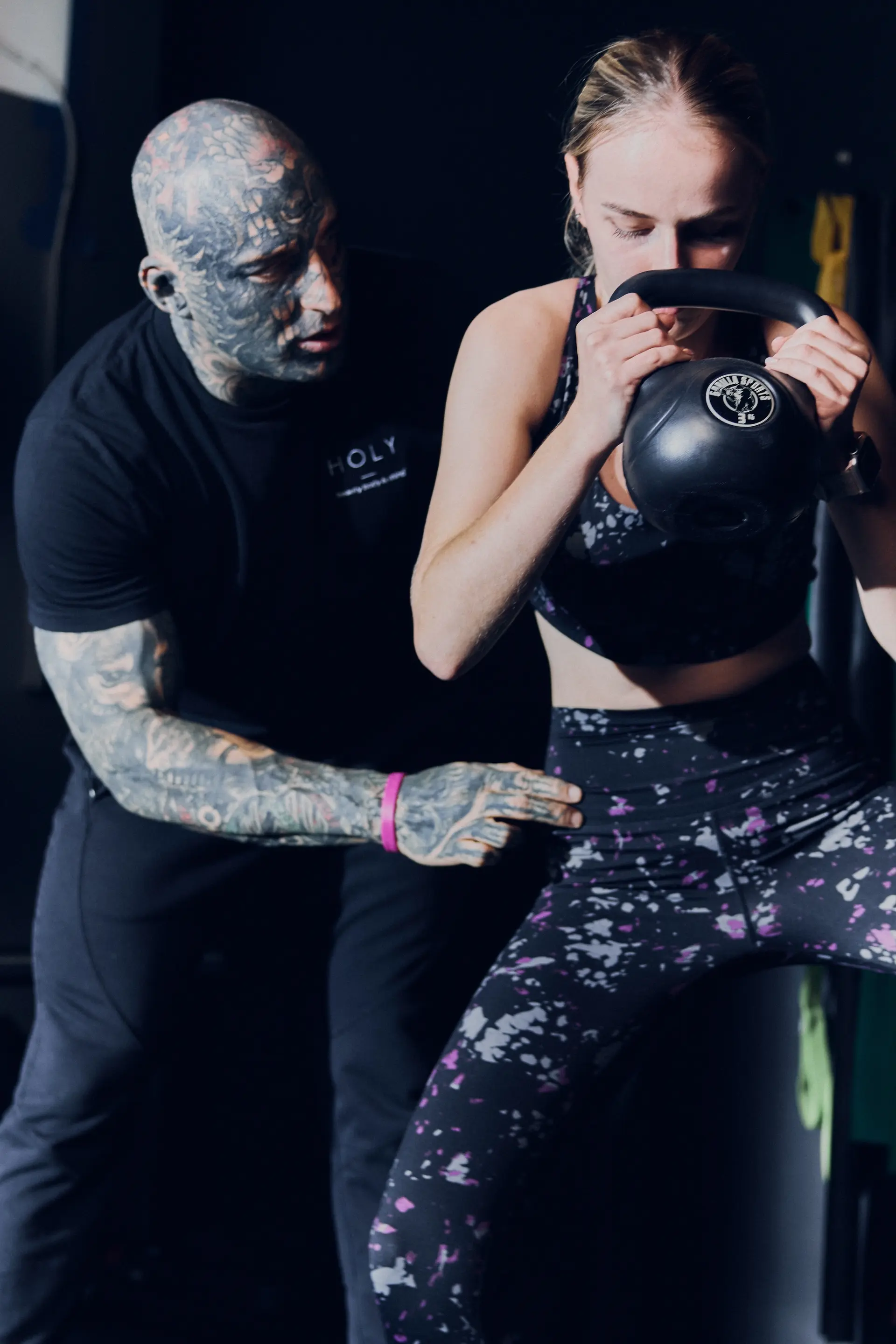 Trener instruuje kobietę trzymającą kettlebell podczas ćwiczenia przysiadu.