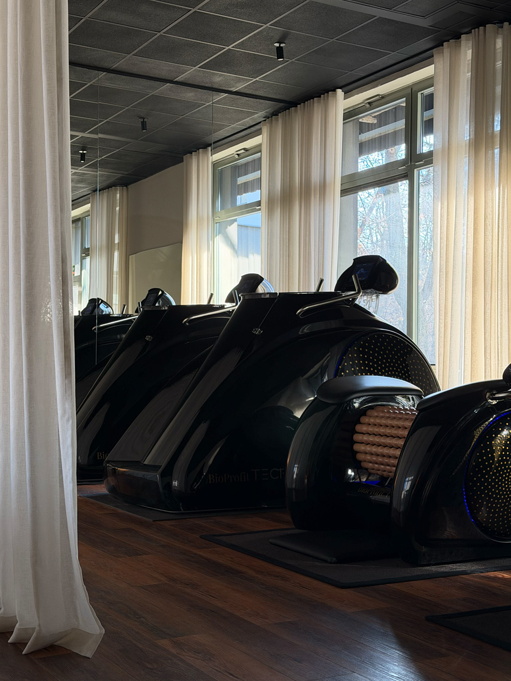 Kobieta ćwicząca rozciąganie w pozycji psa z głową w dół na macie, asystowana przez trenerkę w białej koszulce.