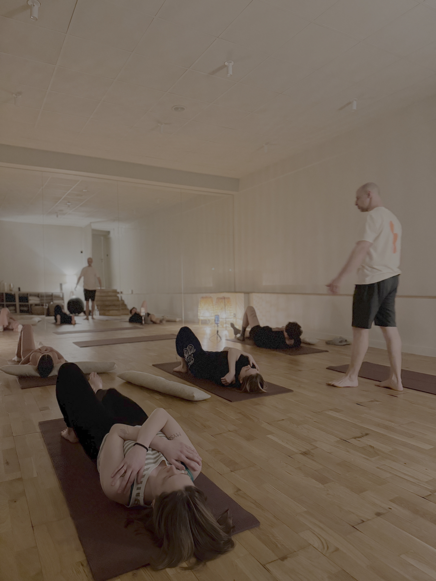 Kobieta ćwicząca rozciąganie w pozycji psa z głową w dół na macie, asystowana przez trenerkę w białej koszulce.