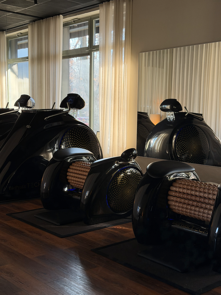 Kobieta ćwicząca rozciąganie w pozycji psa z głową w dół na macie, asystowana przez trenerkę w białej koszulce.