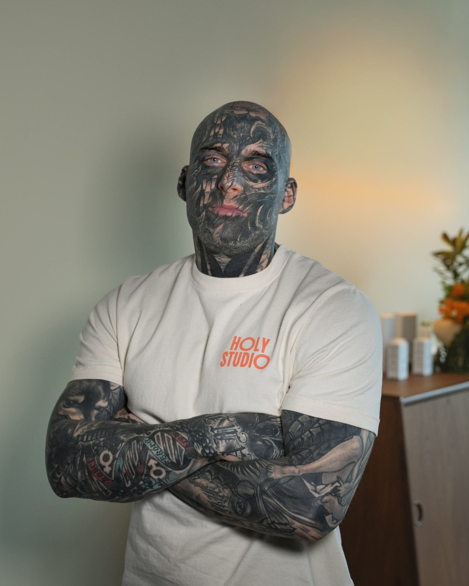 Mężczyzna z tatuażem ubrany w czarną koszulkę z napisem HOLY