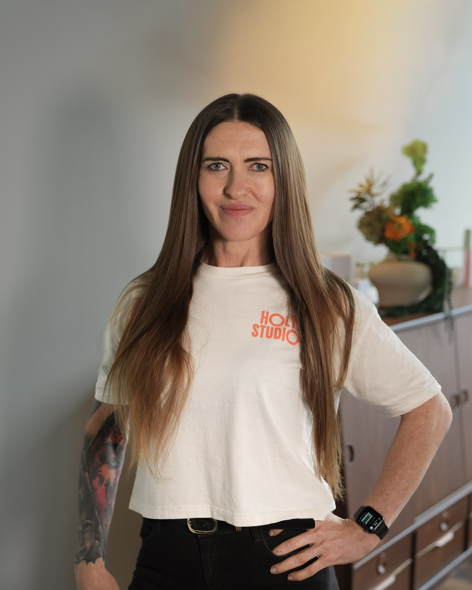 Dwie kobiety podają sobie ręce na powitanie przy białym biurku, w tle wazon z kolorowymi kwiatami.