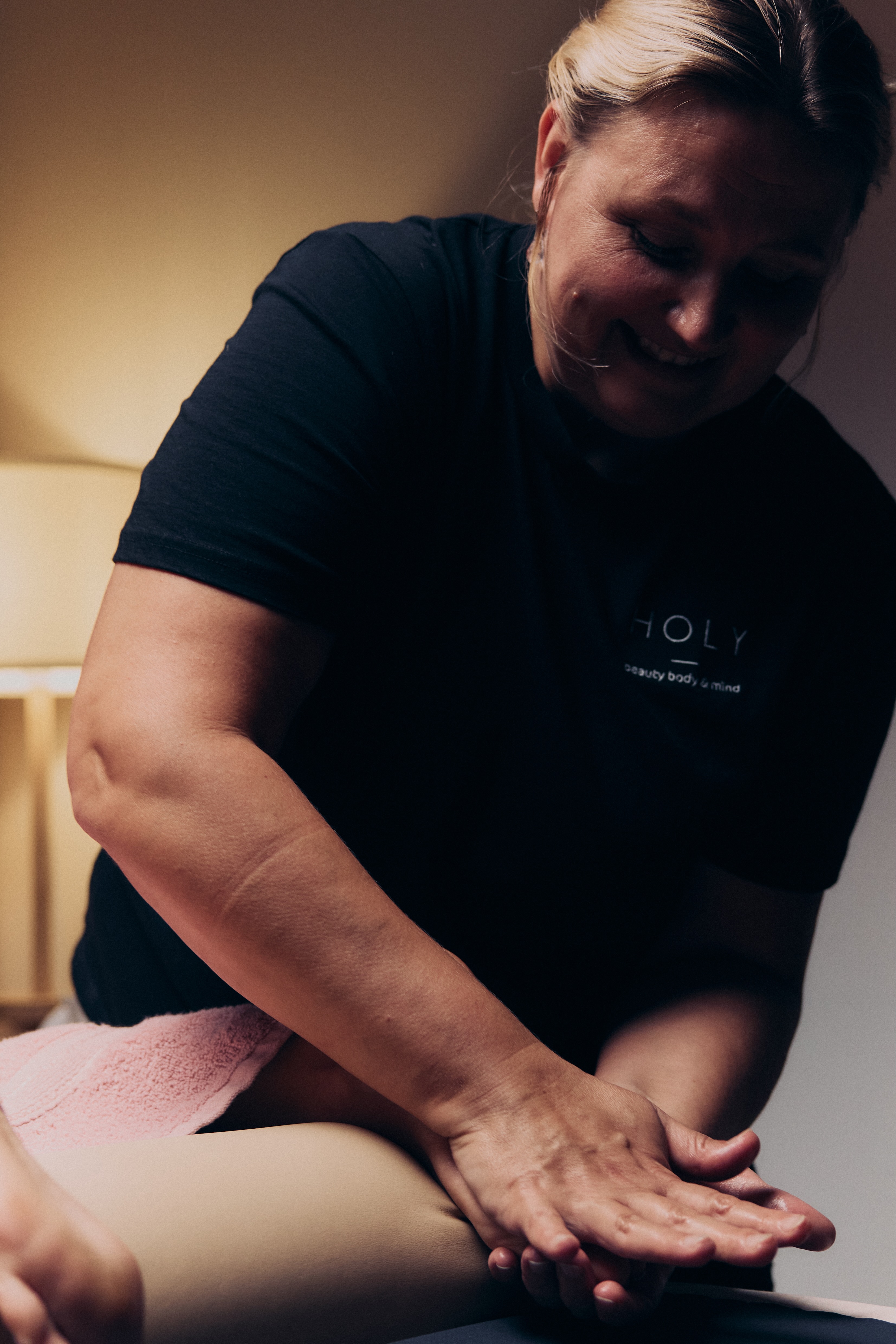 Kobieta ćwicząca rozciąganie w pozycji psa z głową w dół na macie, asystowana przez trenerkę w białej koszulce.