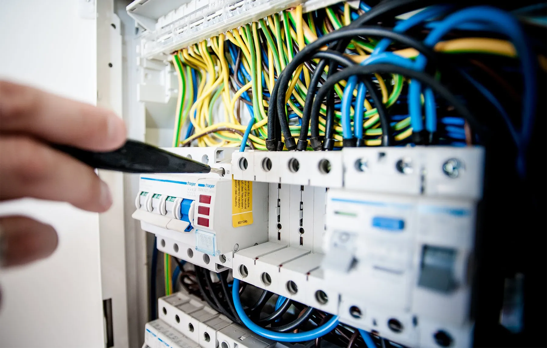 Hand using a tool to adjust wires in an electrical panel with colorful cables.