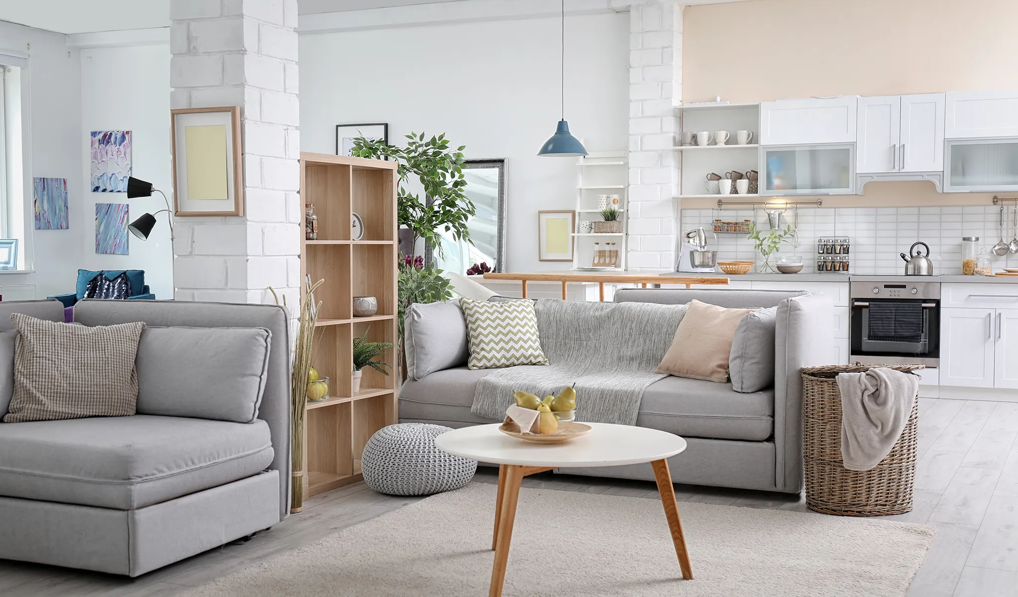 A modern living room and kitchen with gray sofas, a small table, and white cabinets.