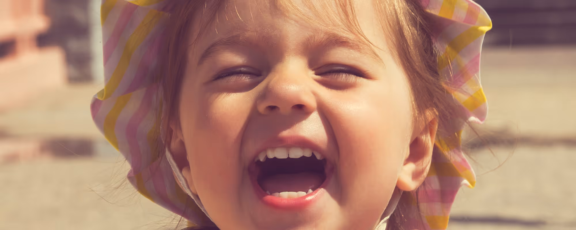 Young child with a wide smile and striped hat, laughing joyfully.