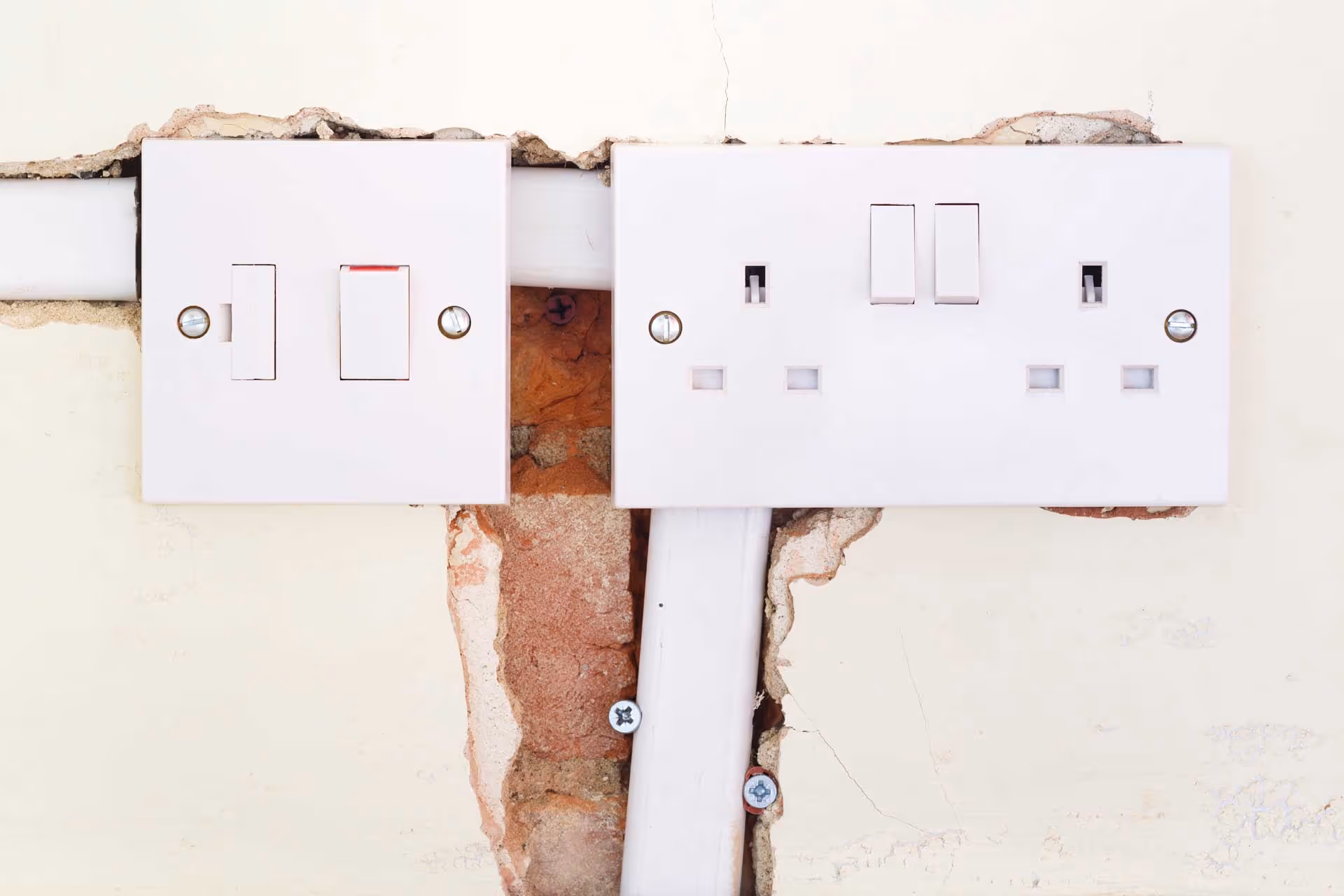Two white electrical switches and sockets on a wall with exposed brick and wiring.