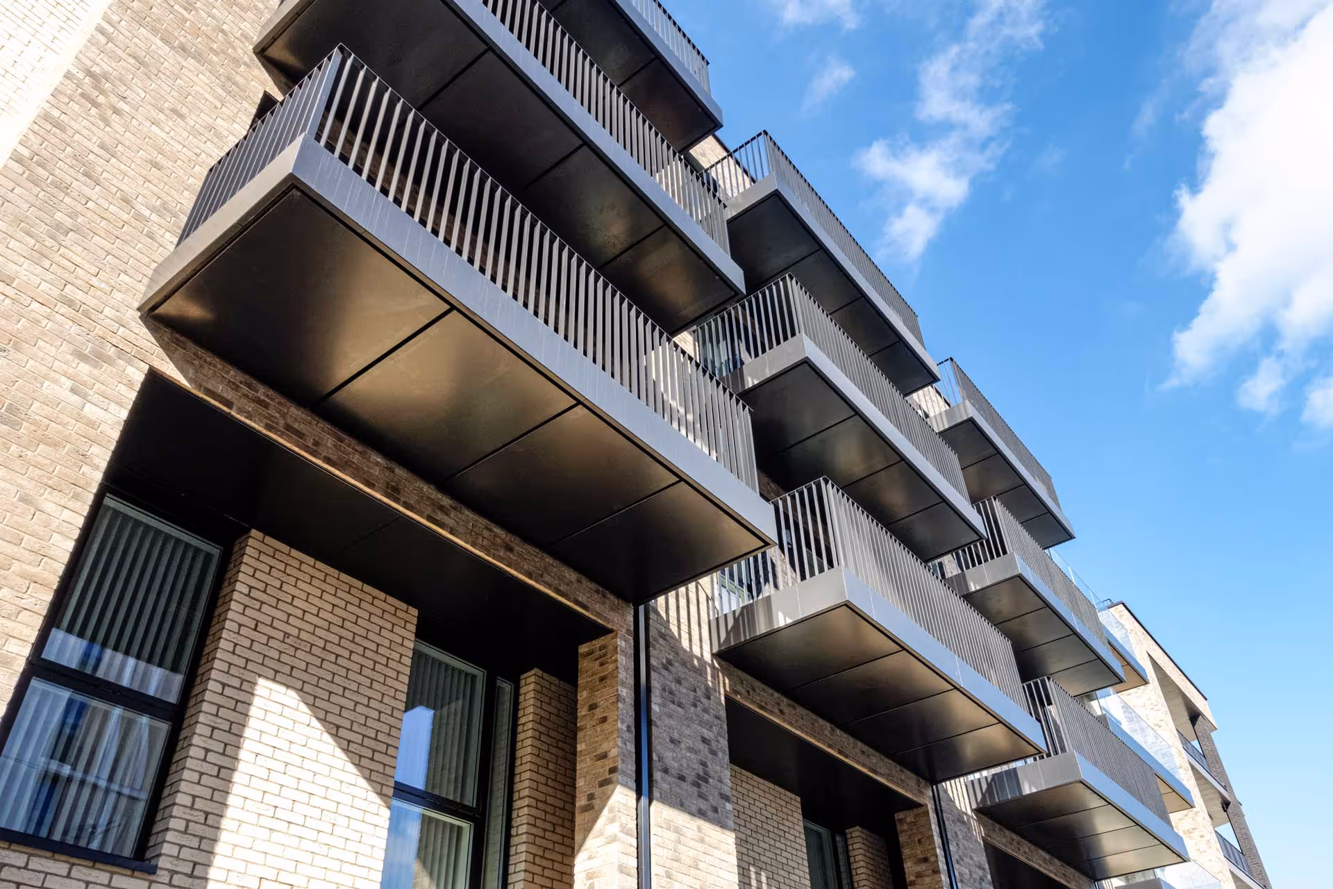 A modern apartment building with multiple balconies against a blue sky background.