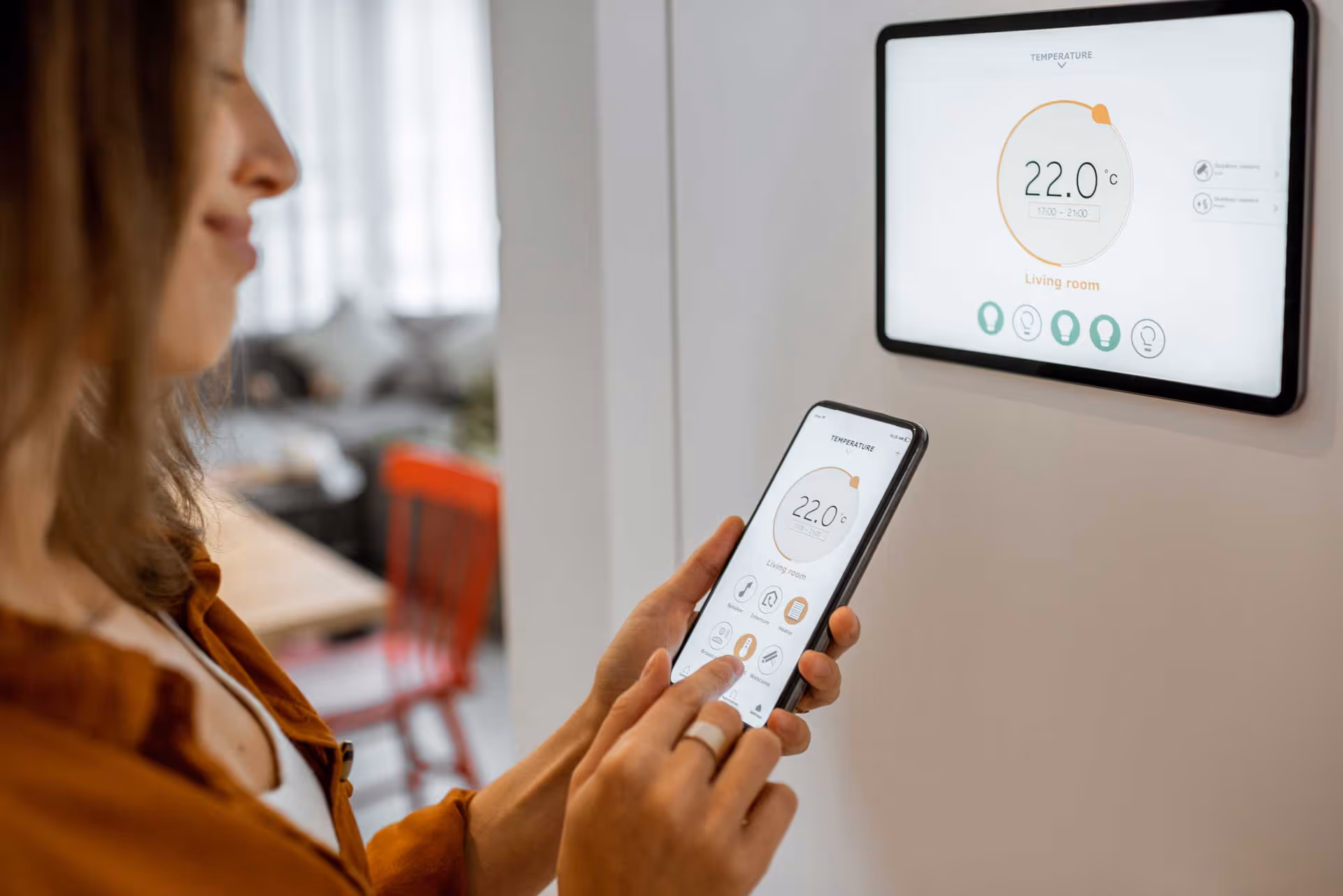 A woman adjusts a smart home thermostat using a smartphone app indoors.