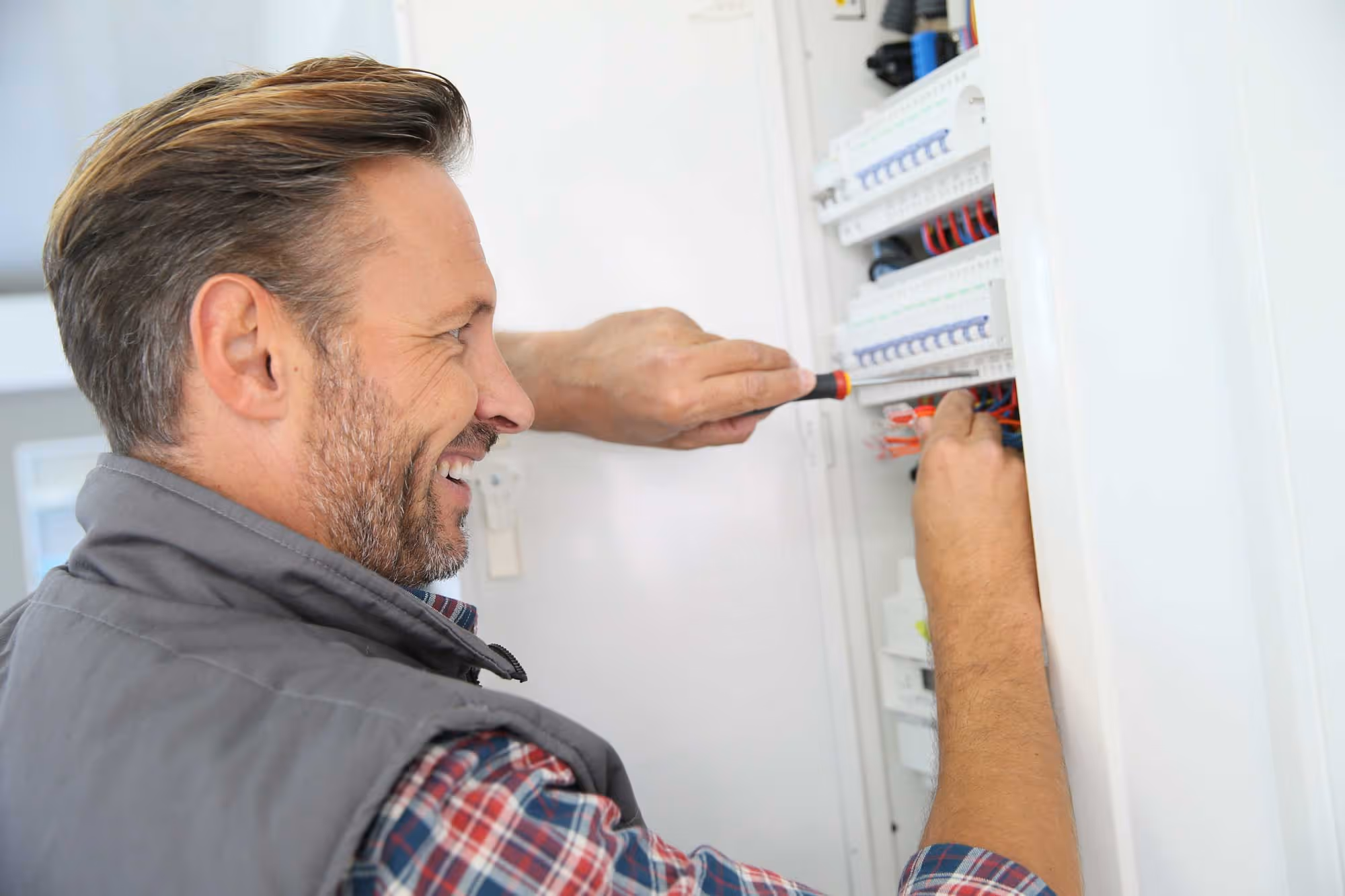 Electrician using a screwdriver to work on a circuit breaker panel.