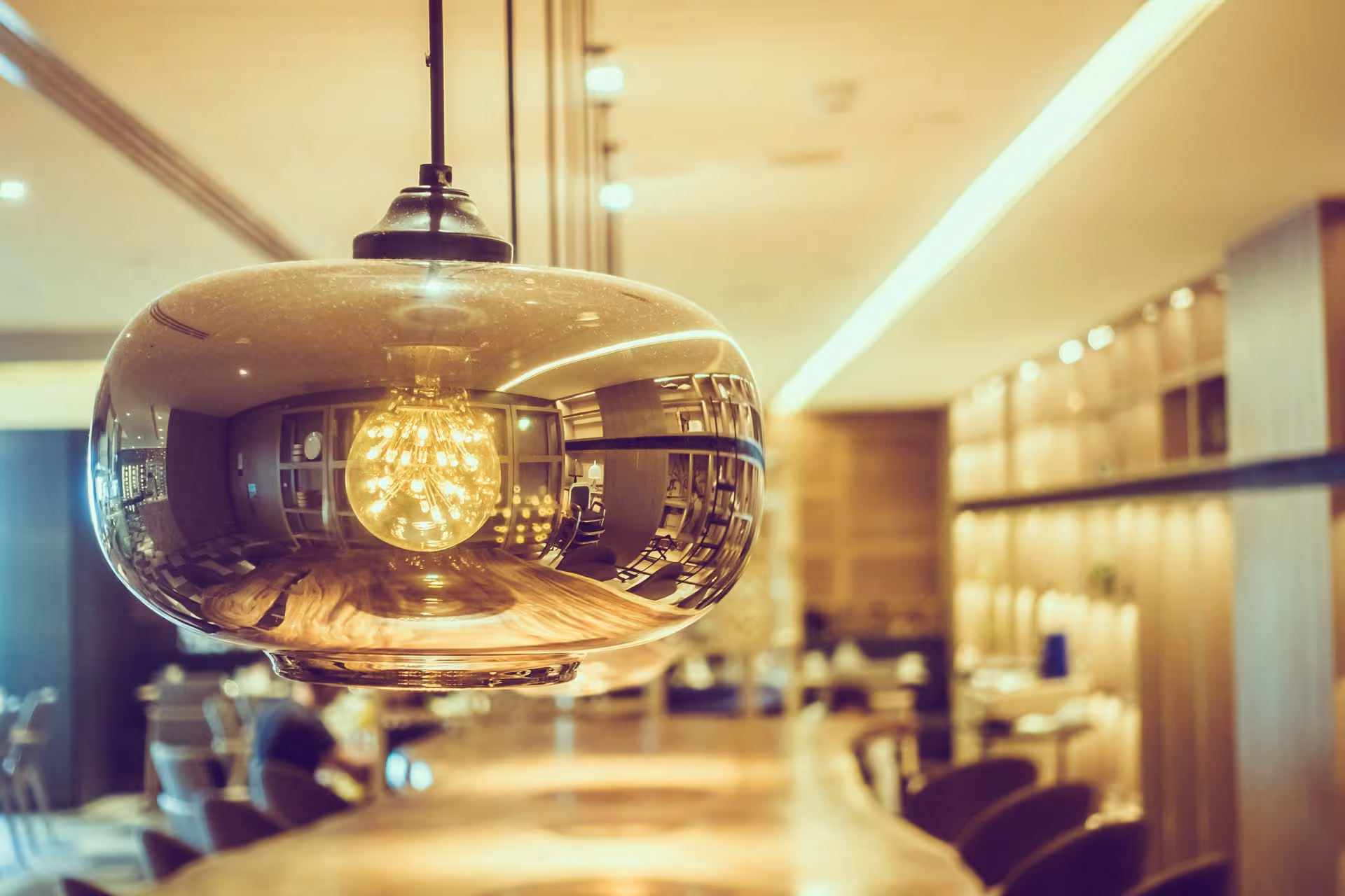 A round light fixture hangs above a wooden table in a warmly lit room.