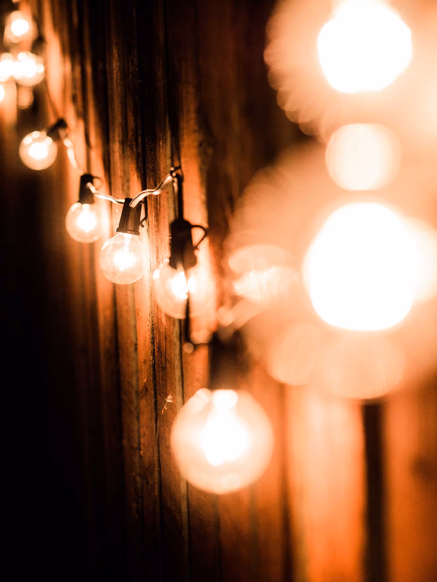 String of round light bulbs hanging on a wooden wall, softly glowing at night.