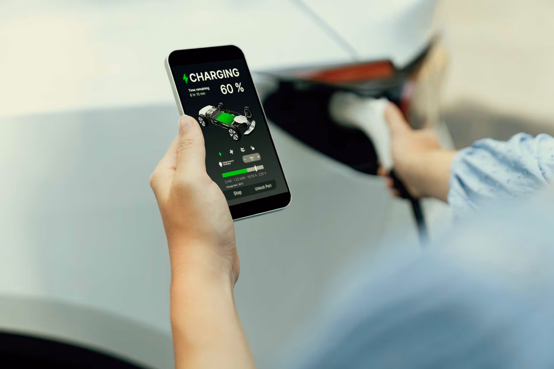 Person holding a phone showing electric car charging progress at 60% while plugging in the car.